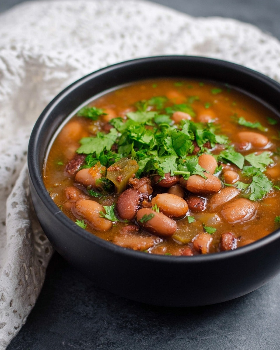 A black bowl filled with a brown bean soup that has a mix of whole and soft beans in the broth, showing different shades of brown and some green pieces inside. The soup is topped with fresh, bright green cilantro leaves scattered on the surface. The bowl is placed on a white marbled texture with a white patterned cloth partially visible in the background. The overall look is warm and comforting with a focus on the rich texture of the beans and fresh herbs. photo taken with an iphone --ar 4:5 --v 7
