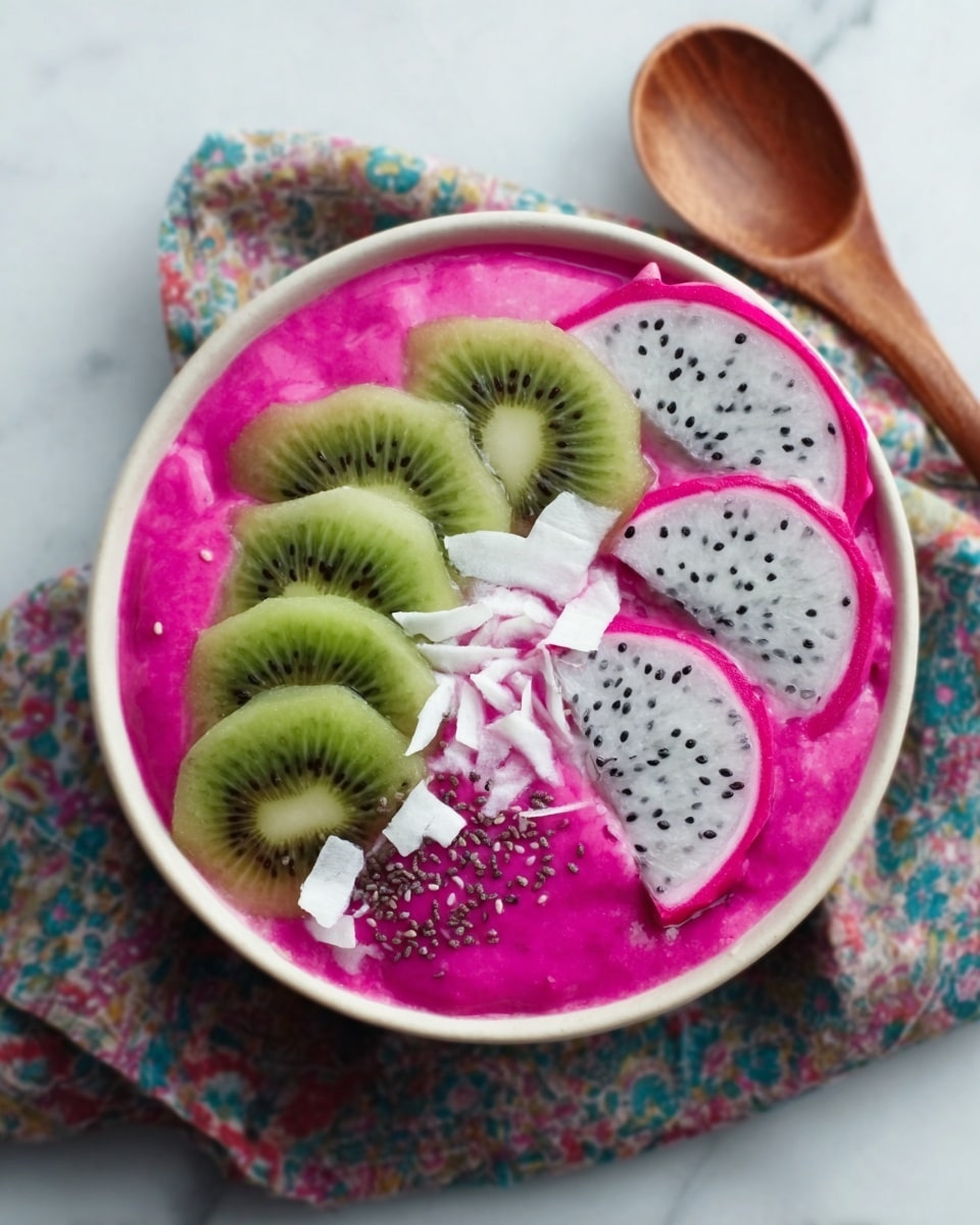 A white bowl sits on a colorful cloth with a wooden spoon beside it, all on a white marbled surface. The bowl is filled with a bright pink smoothie that looks creamy and smooth, covering the bottom layer. On top of the pink smoothie, there are thin slices of light green kiwi arranged in a curved line on one side and two pieces of white dragon fruit with black seeds on the other side. White coconut flakes are spread over the center, along with small dark chia seeds sprinkled lightly across the smoothie. Photo taken with an iphone --ar 4:5 --v 7