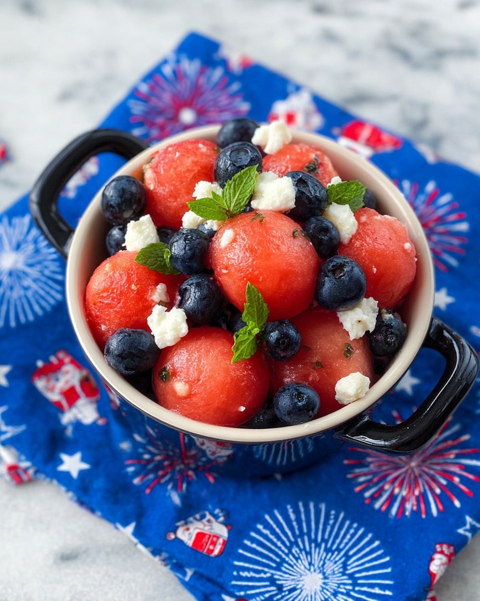 A small white bowl with black handles is filled with three main layers of fresh fruit: smooth, round red watermelon balls on top and throughout, glossy dark blueberries scattered among them, and white crumbled cheese pieces mixed in for texture and color contrast, along with small green mint leaves adding a touch of freshness. The bowl sits on a bright blue cloth decorated with red and white fireworks and cartoon characters, all placed on a white marbled surface. photo taken with an iphone --ar 4:5 --v 7