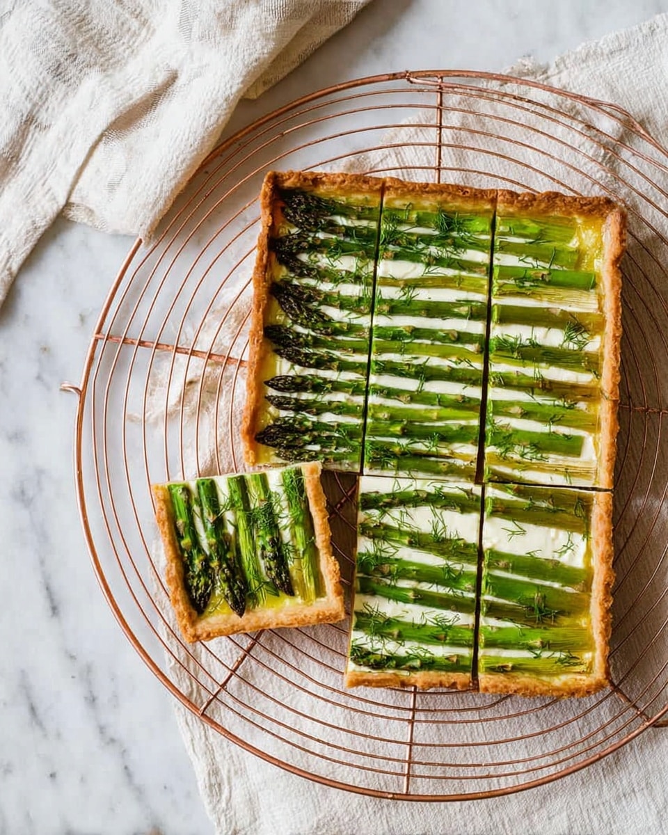 A rectangular tart with a golden brown thick crust edges, topped with a neat layer of green asparagus spears laid out lengthwise, alternating with a creamy white cheese layer underneath. Fresh green dill leaves are sprinkled lightly on top. The tart is cut into nine square pieces with two pieces slightly pulled out from the rest. It sits on a round copper wire cooling rack placed on a white marbled surface, with a light cream and beige striped cloth partially visible in the background. Photo taken with an iphone --ar 4:5 --v 7