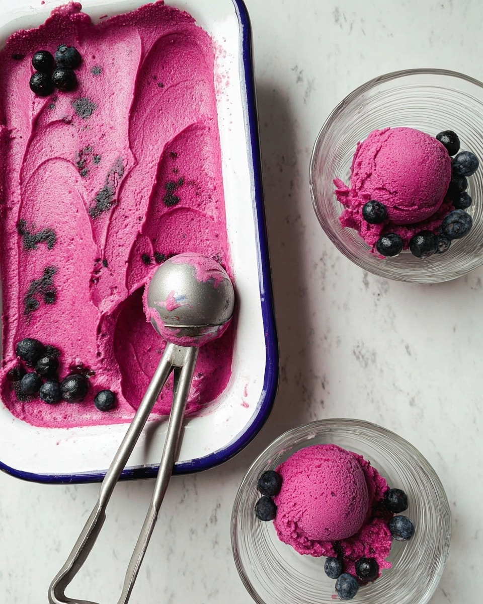 The image shows a white dish with a dark blue rim holding bright purple ice cream, smooth in texture with a few small black berries on top and embedded in the ice cream. Two clear glass bowls on the right contain single, round scoops of the same purple ice cream, each scoop garnished with a small cluster of black berries. A metal ice cream scoop with traces of the purple ice cream inside is placed between the dish and the bowls. The scene is set on a white marbled surface, giving a clean and bright background. photo taken with an iphone --ar 4:5 --v 7