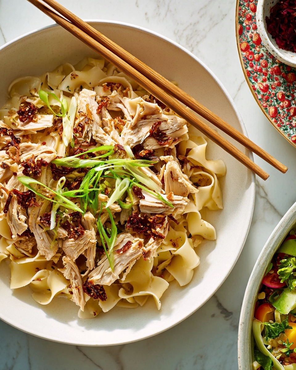 The image shows a bowl filled with wide, flat noodles that are light beige and slightly shiny, mixed with pieces of shredded cooked chicken that are pale brown and tender-looking. On top, there are crispy, dark golden-brown bits scattered unevenly, adding texture. Thin slices of fresh green onions are sprinkled over everything, giving a fresh green pop of color. Two wooden chopsticks rest on the edge of the white bowl. The bowl is set on a white marbled surface, with part of another bowl visible to the right, containing a colorful salad. Photo taken with an iphone --ar 4:5 --v 7