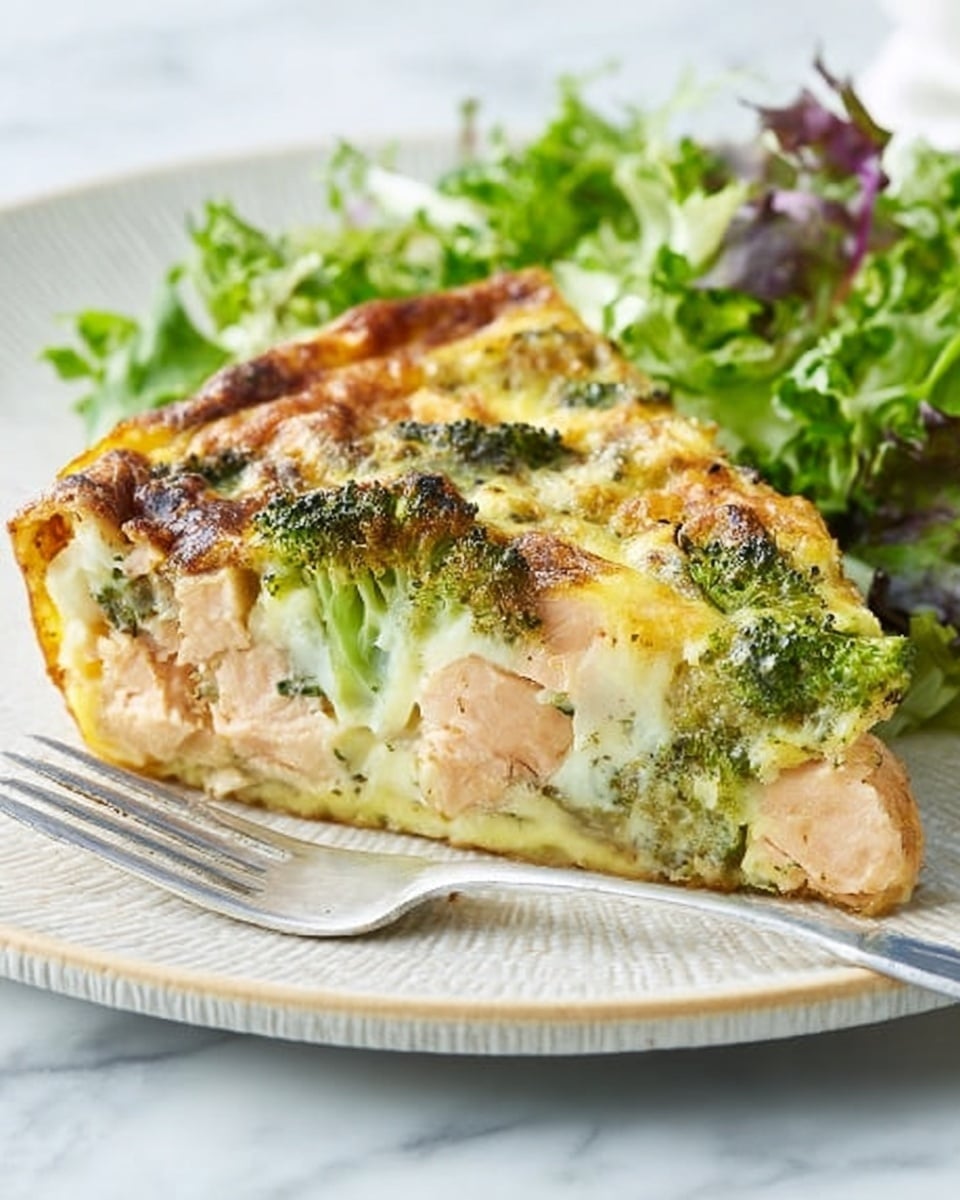 A slice of frittata is placed on a white plate with thin blue stripes around the edge. The frittata slice has three visible layers: a light, creamy, slightly yellow egg base at the bottom; a middle layer containing chunks of pinkish cooked salmon; and a top layer of bright green broccoli pieces and herbs mixed into the yellow, slightly browned cooked eggs. Next to the frittata slice on the plate is a small side of fresh mixed leafy greens in various shades of green and some reddish-purple. A silver fork rests beside the plate on a white marbled surface in soft, natural light, creating a fresh, clean look. Photo taken with an iphone --ar 4:5 --v 7