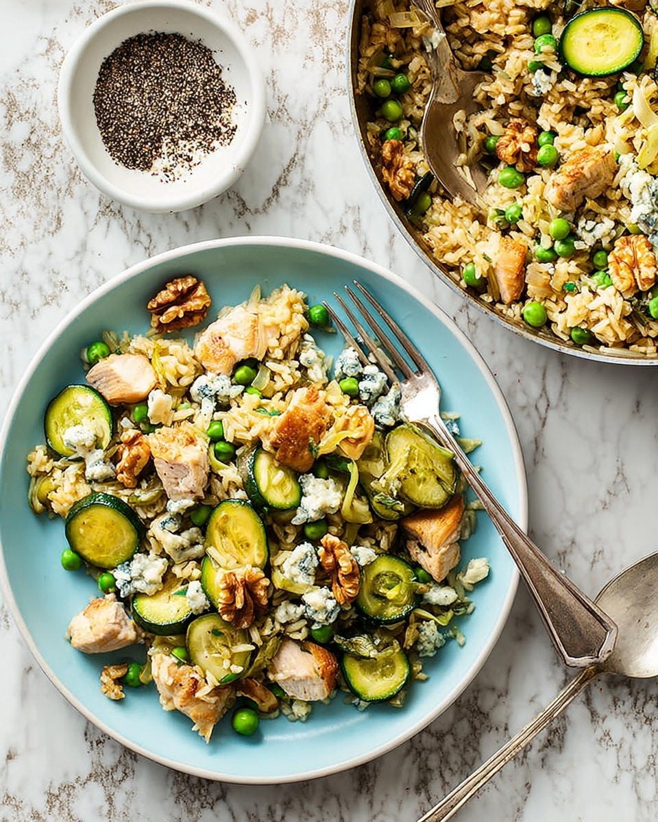 A white round plate filled with a layered dish showing green peas scattered throughout the light brown rice base, with slices of cooked green zucchini, chunks of light golden brown chicken pieces, and small dollops of creamy white cheese mixed with blue accents placed on top along with a few walnut pieces. To the right, part of a stainless steel pan with the same dish is visible, with a metal spoon resting on it. In the top center, a small white bowl contains cracked black and red peppercorns. The whole scene is set on a bright white marbled texture background. photo taken with an iphone --ar 4:5 --v 7