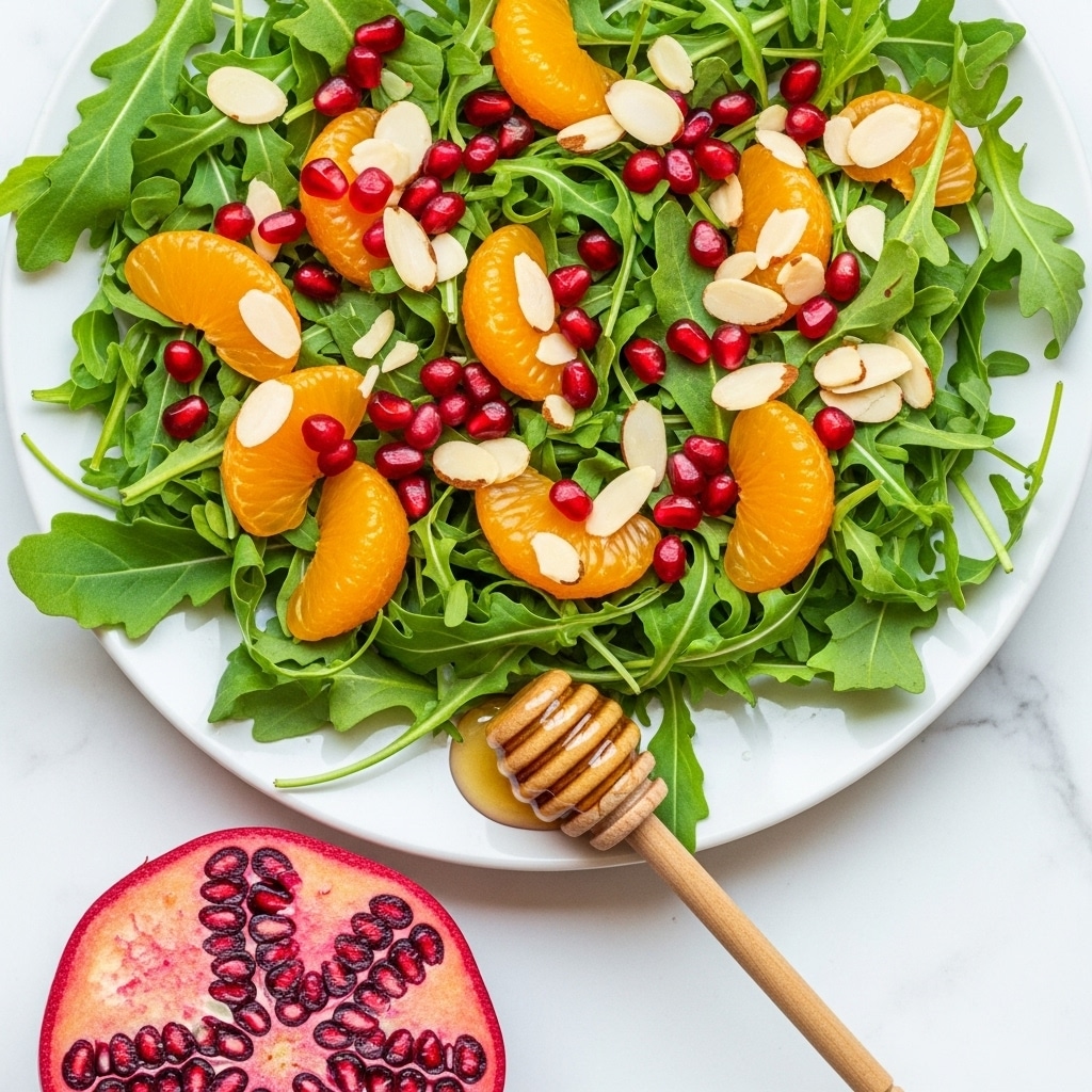 A fresh salad arranged on a white rectangular plate features a mix of dark green leafy greens as the base layer, topped with bright orange mandarin segments scattered throughout. There are small shiny red pomegranate seeds sprinkled over the greens, adding pops of color. Thin, off-white almond flakes are lightly scattered on top. At the front right corner of the plate, there is a cluster of pomegranate seeds still attached to a piece of pomegranate fruit. A wooden honey dipper rests at the bottom left of the plate with some honey pooling beneath it. The plate is set on a white marbled surface. photo taken with an iphone --ar 4:5 --v 7