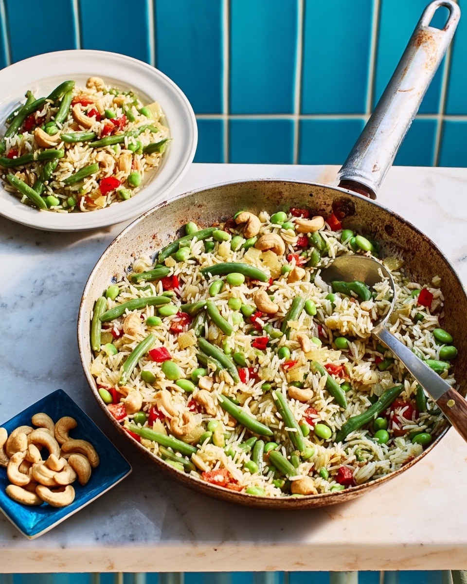 The image shows a large pan filled with a colorful mix of cooked rice and green vegetables including snap peas, edamame, and sliced green beans, with small pieces of red bell pepper scattered on top. Next to the pan, there is a white bowl also filled with the same vegetable rice mixture. To the side, a small white plate holds a pile of light brown cashew nuts. The pan and the bowl are placed on a white marbled surface with a bright blue tile wall in the background. A metal spoon is resting inside the pan, slightly lifting some of the rice and vegetables. Photo taken with an iphone --ar 4:5 --v 7