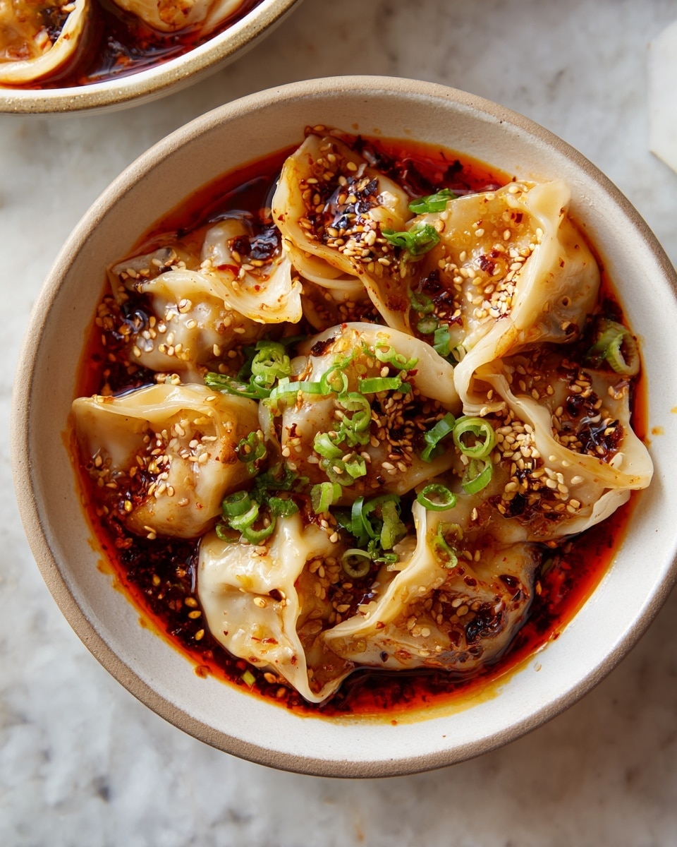 The dish shows a bowl filled with dumplings in a red spicy sauce. The dumplings are light beige and soft-looking, sitting in a thick, oily red sauce with visible chili flakes and seeds. On top, there are chopped green onions and white sesame seeds scattered evenly, adding color contrast. The bowl is white with a blue textured pattern inside, and it is set on a white marbled surface. A woman's hand is just touching the edge of the bowl. Photo taken with an iphone --ar 4:5 --v 7