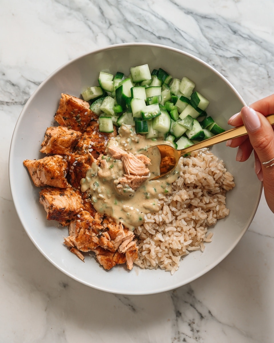 A white bowl sits on a white marbled surface, filled with three clear layers. The bottom layer is light brown rice with a soft, fluffy texture. On top of the rice to one side, there are small cubes of fresh, green cucumber. Next to the cucumber, there is a serving of crispy, golden-brown cooked salmon with a slightly shiny surface. In the center, there is a creamy, light brown sauce drizzled over the rice, creating smooth texture contrasts. A woman's hand is holding the bowl with a gold spoon lifting some food. Photo taken with an iphone --ar 4:5 --v 7