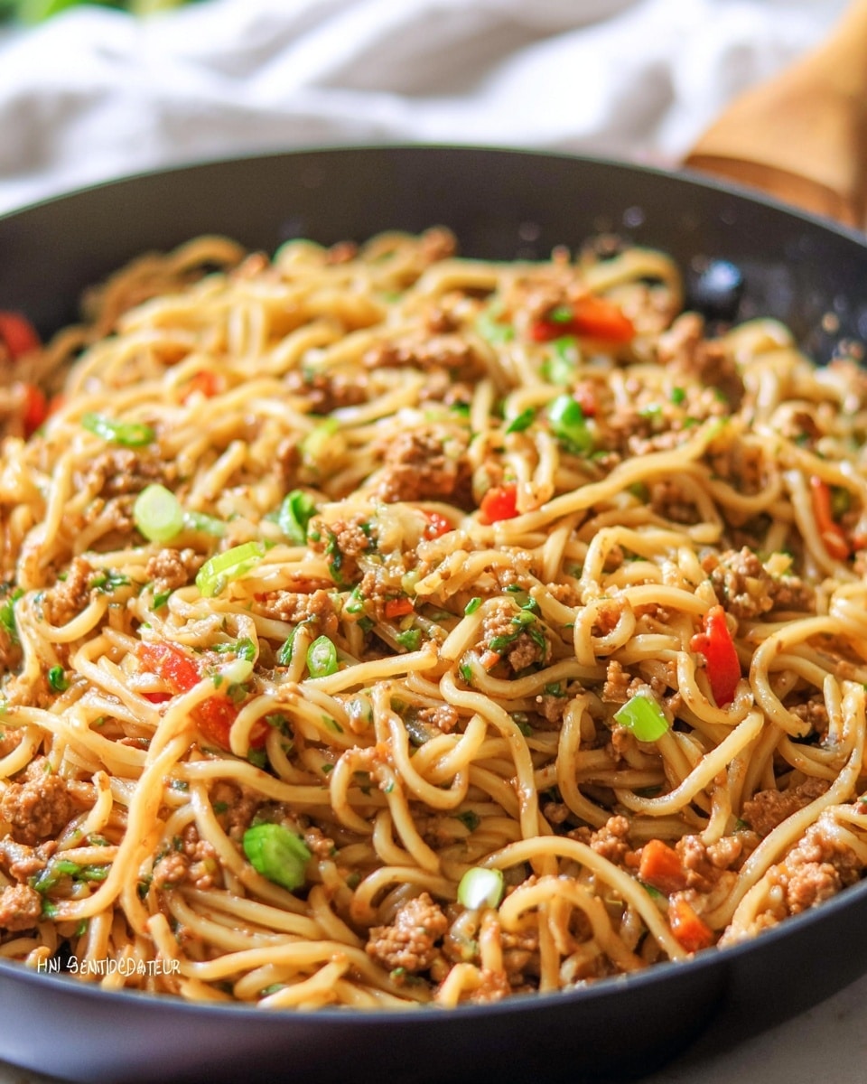 A close-up view of a black pan filled with a single layer of Asian-style noodles mixed with small pieces of ground meat and diced red and green vegetables, all coated in a light brown sauce. The noodles have a smooth and slightly shiny texture, interspersed with chopped green herbs and small bits of crushed nuts scattered on top. The pan is set against a blurred white marbled background with a hint of an out-of-focus drink glass in the upper right corner. The overall scene highlights the warm, comforting mix of textures and colors in the dish, photo taken with an iphone --ar 4:5 --v 7