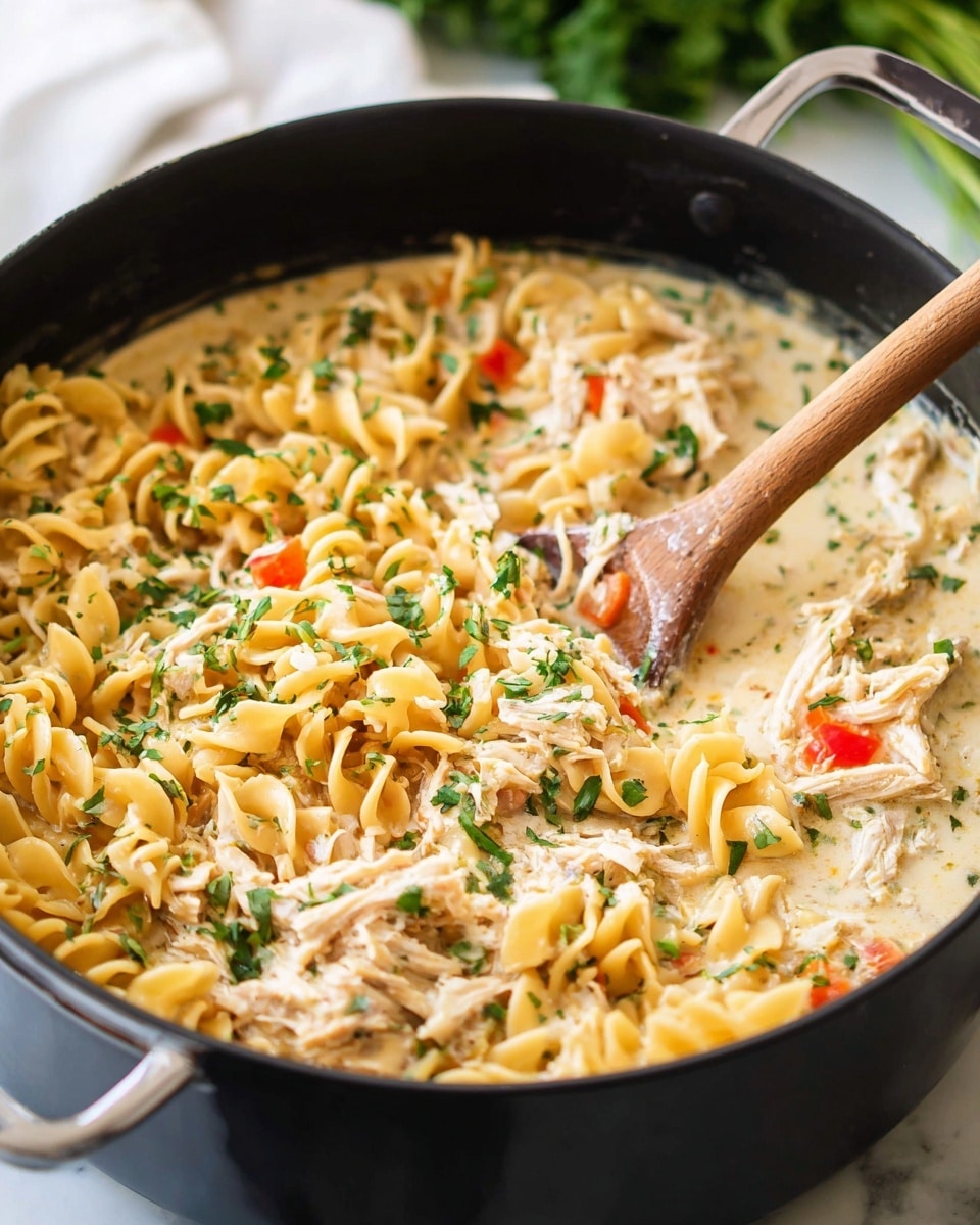 A close-up view inside a white pot filled with a creamy pasta dish consisting of three main layers: at the bottom, a wavy egg noodle layer in pale yellow with some softness visible; the middle layer is tender shredded chicken in light beige mixed with small pieces of diced red bell peppers; the top layer is a smooth and rich creamy sauce with a light beige color, sprinkled with chopped green herbs on top adding freshness and texture, with a wooden spoon partially dipped into the food, stirring gently. The scene rests on a white marbled surface in soft daylight. photo taken with an iphone --ar 4:5 --v 7