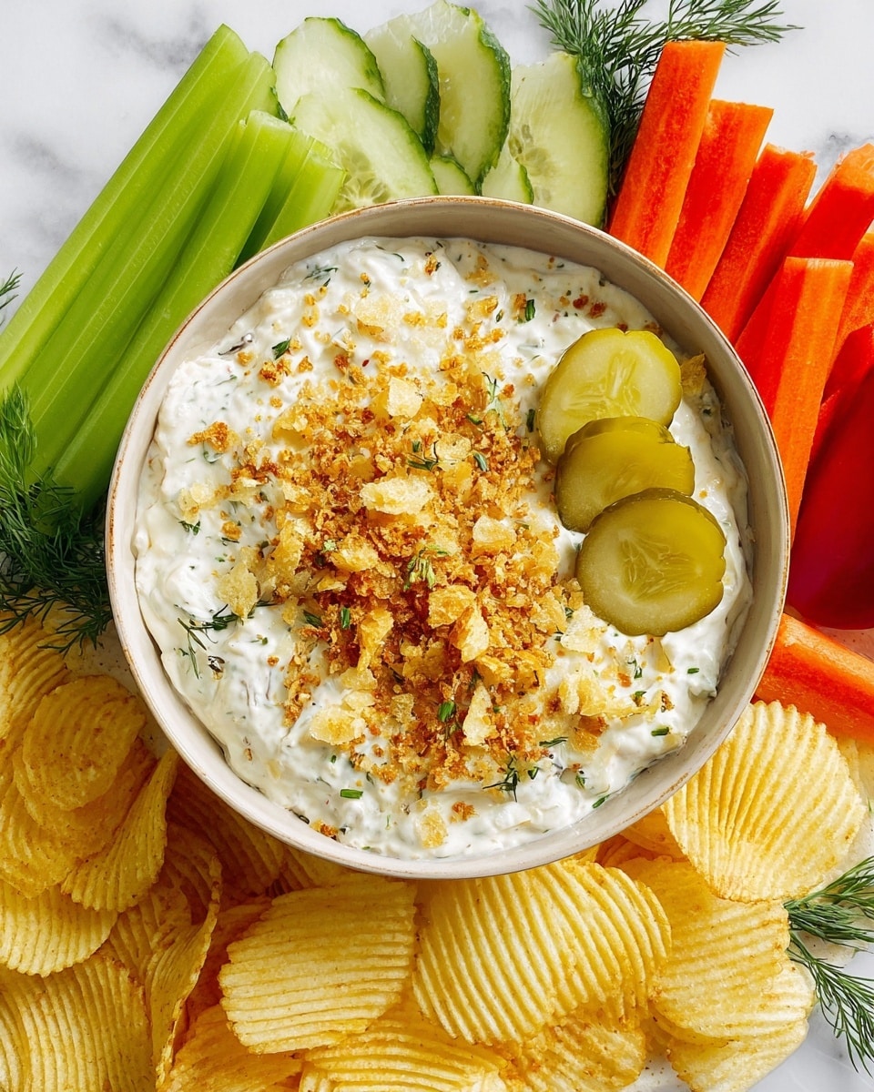 A white bowl filled with creamy dip topped with golden brown crunchy crumbs, chopped light yellow pickles, and green dill sprigs scattered on the surface. Three ridged pickle slices rest on one side near the edge. Surrounding the bowl are fresh sticks of celery, orange carrots, green cucumber, and red bell pepper, all crisp and neatly arranged. Below the bowl are ridged, pale yellow potato chips forming a base layer. The setting is on a white marbled surface. photo taken with an iphone --ar 4:5 --v 7