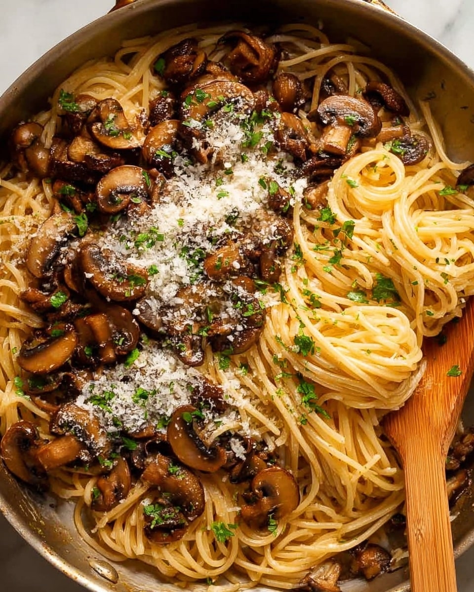 This image shows a close-up view of a pan filled with spaghetti pasta mixed with sautéed mushroom slices. The bottom layer is light yellow spaghetti strands, soft in texture and loosely piled. The top layer has dark brown, glossy, cooked mushroom slices evenly spread over the pasta. Small green parsley leaves are scattered lightly on top for color. Some grated white cheese is sprinkled in small patches on the mushrooms. The pan itself is metallic with a wooden spatula partially visible on the right side. The background is a white marbled texture. Photo taken with an iphone --ar 4:5 --v 7