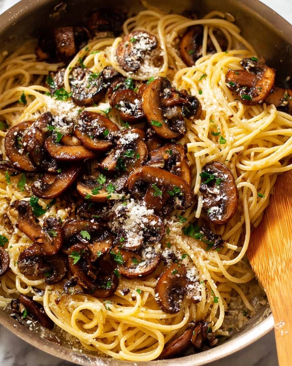 A close-up view of a pan filled with cooked spaghetti pasta as the base layer, light golden in color and soft in texture. On top, there is a layer of sautéed mushrooms, dark brown and slightly glossy from cooking, scattered evenly across the pasta. Small sprinkles of finely grated white cheese are spread over the mushrooms, with chopped green herbs added for color and freshness. A wooden spoon is partly visible on the right side, stirring the pasta. The entire scene is set against a white marbled texture. photo taken with an iphone --ar 4:5 --v 7