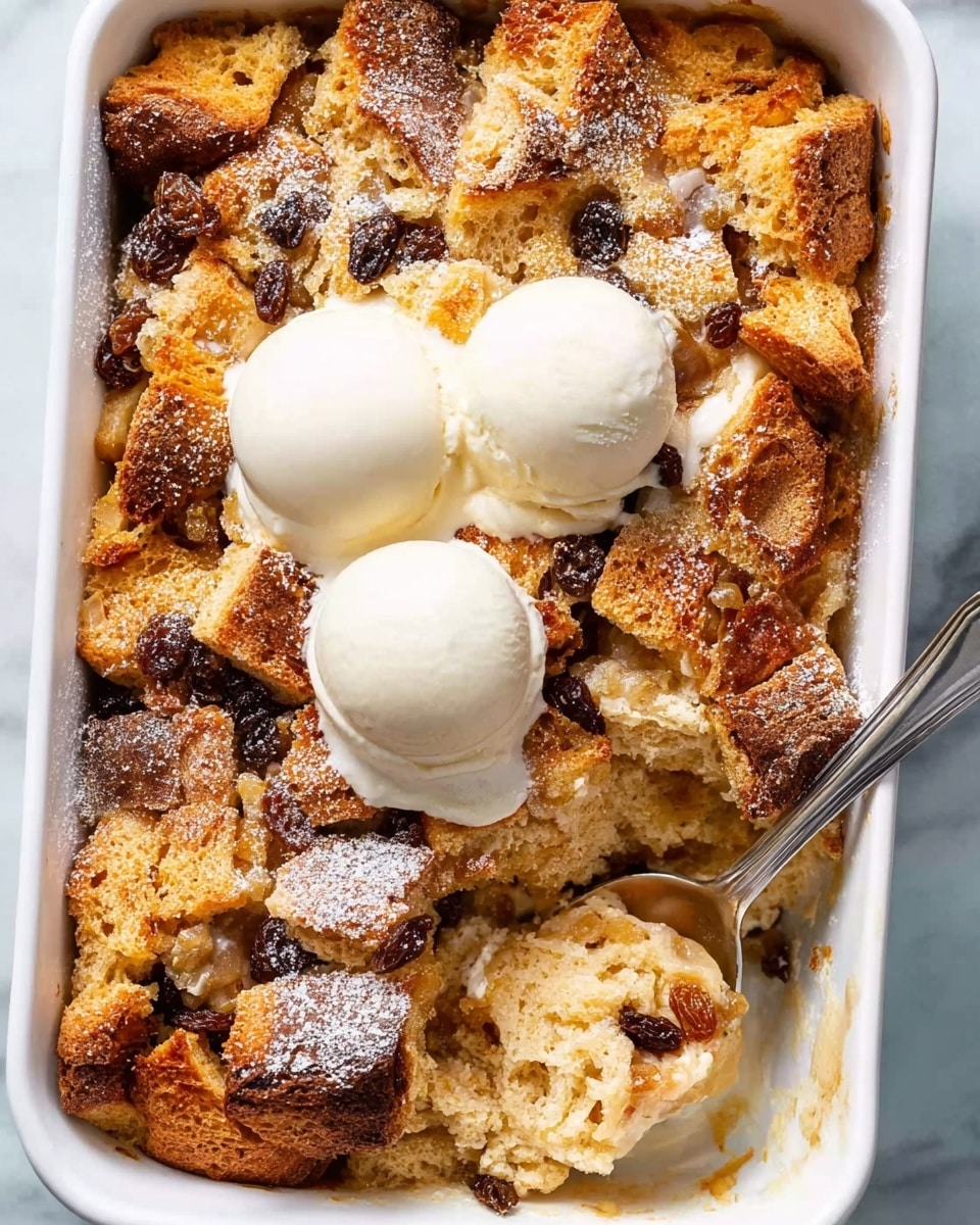 A white baking dish filled with a golden-brown bread pudding topped with raisins is sprinkled with powdered sugar. On top, there are three round scoops of white vanilla ice cream melting slightly into the warm dessert. A silver spoon is scooping out a portion from the right side, revealing a soft, moist interior with a light, fluffy texture, and visible raisins. The dish is placed on a white marbled surface. photo taken with an iphone --ar 4:5 --v 7